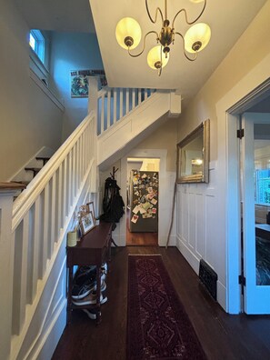 A staircase with a white railing, a chandelier, a hallway with a patterned rug, and a refrigerator covered in photos. - Cozy East Van detached home with large backyard (Vancouver)