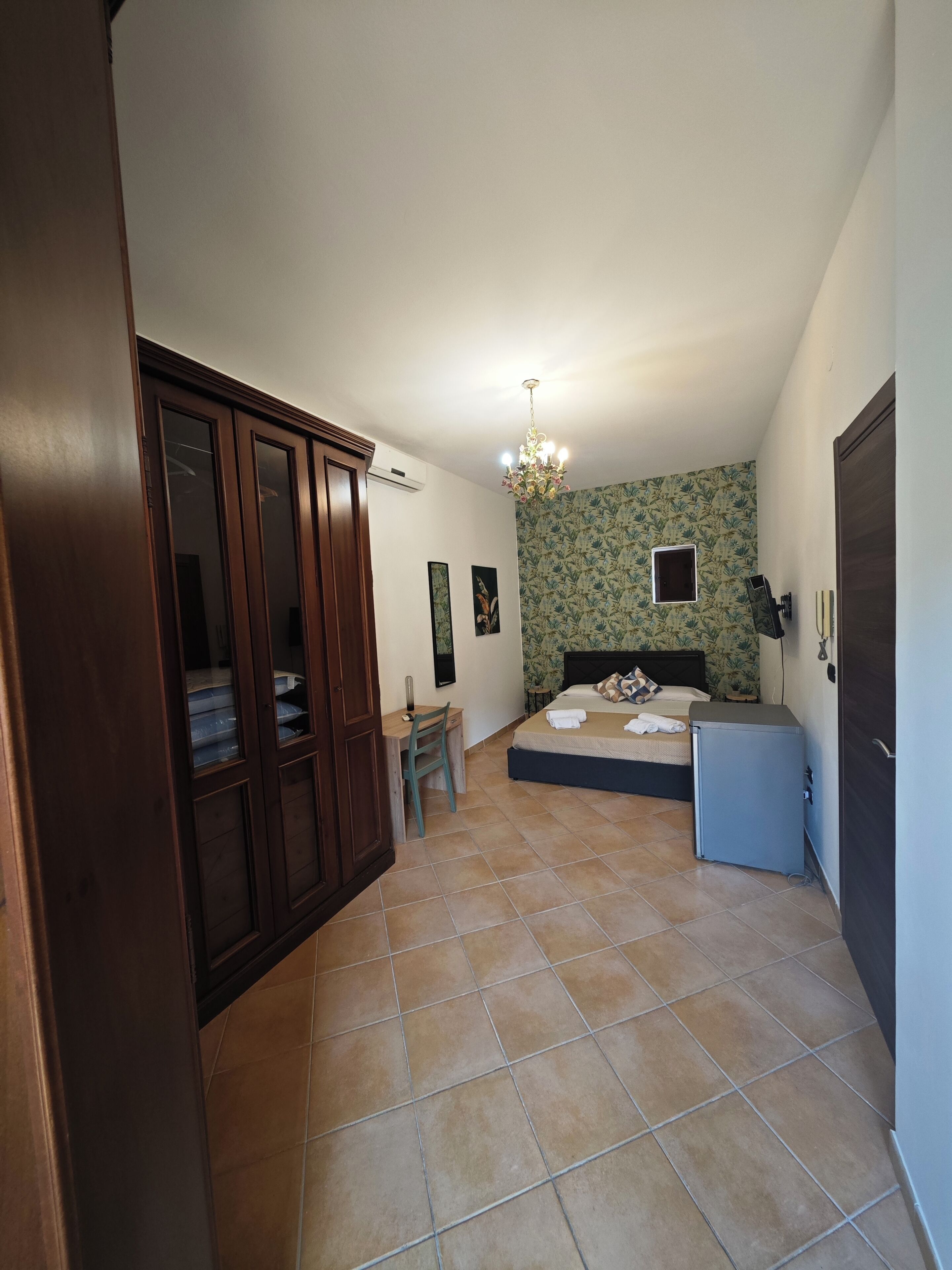 A bedroom with a bed, a desk, a chair, a wardrobe, and a small cabinet.