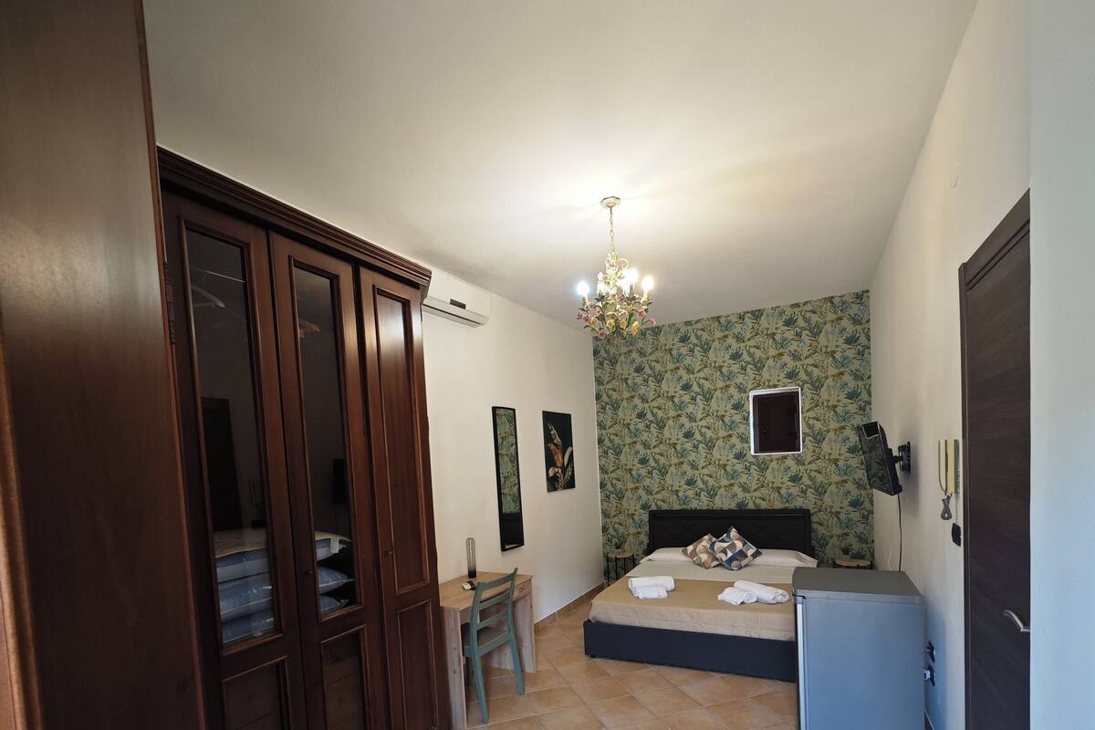 A bedroom with a bed, a desk, a chair, a wardrobe, and a small cabinet.