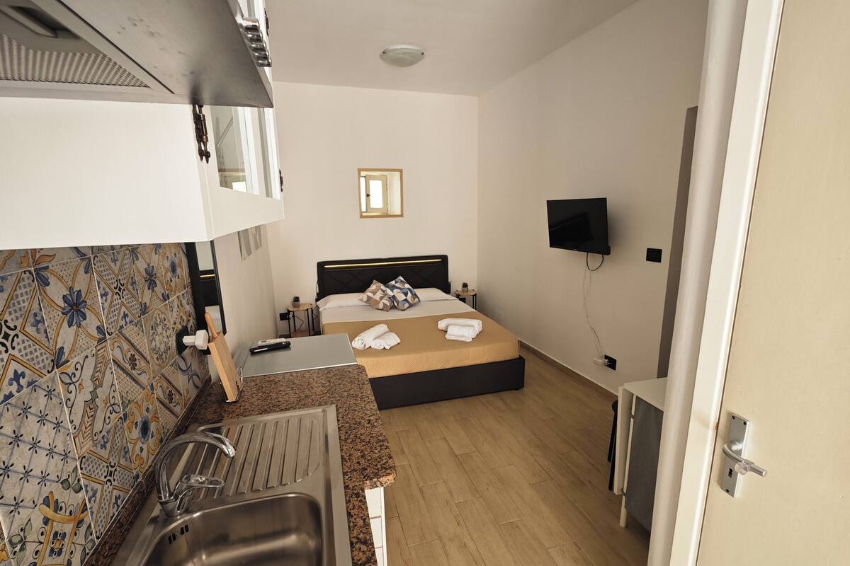 A compact hotel room with a kitchenette, a bed, a TV, and a bathroom.