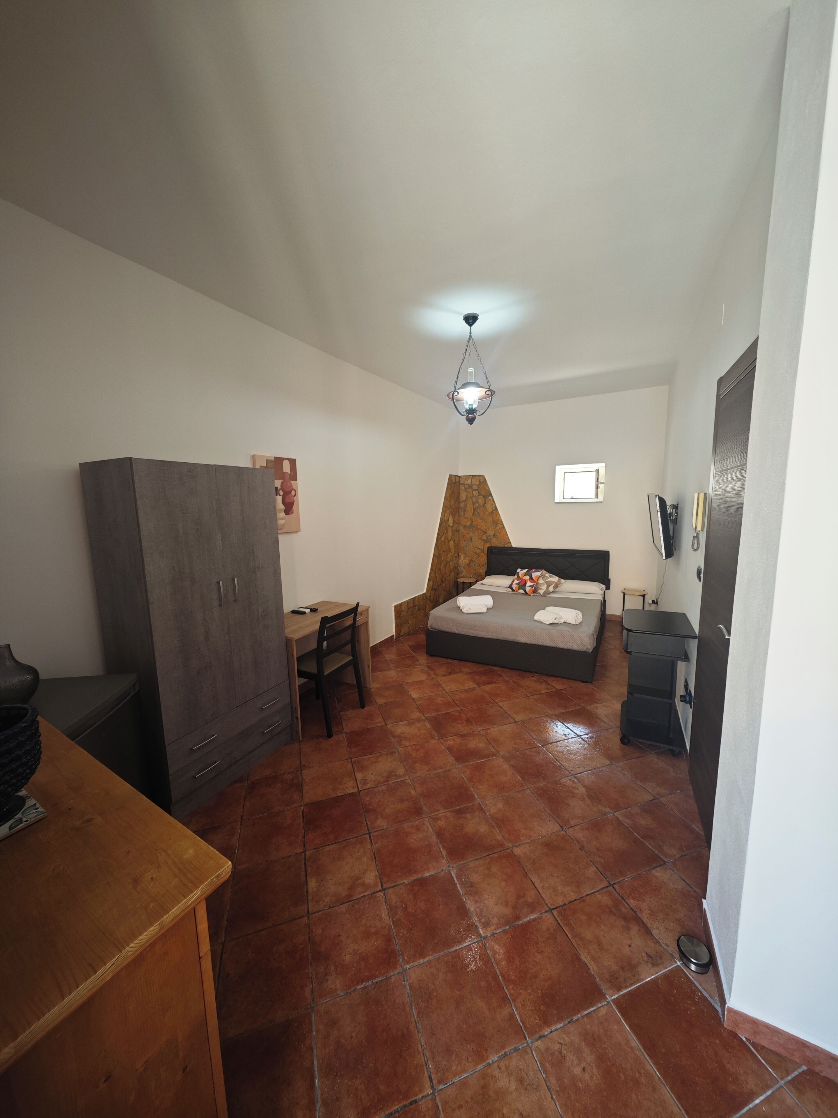 A bedroom with a bed, a desk, a wardrobe, a TV, and a bathroom.
