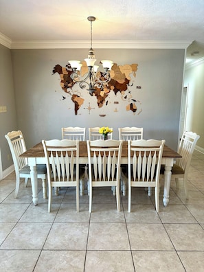 A dining room with a world map wall, a chandelier, and a wooden table with white chairs.