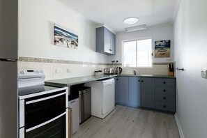 Una cocina compacta con estufa, lavavajillas y ventana.