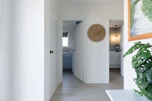 Een gang die uitkomt in een keuken met witte wanden, een houten vloer en een wanddecoratie.