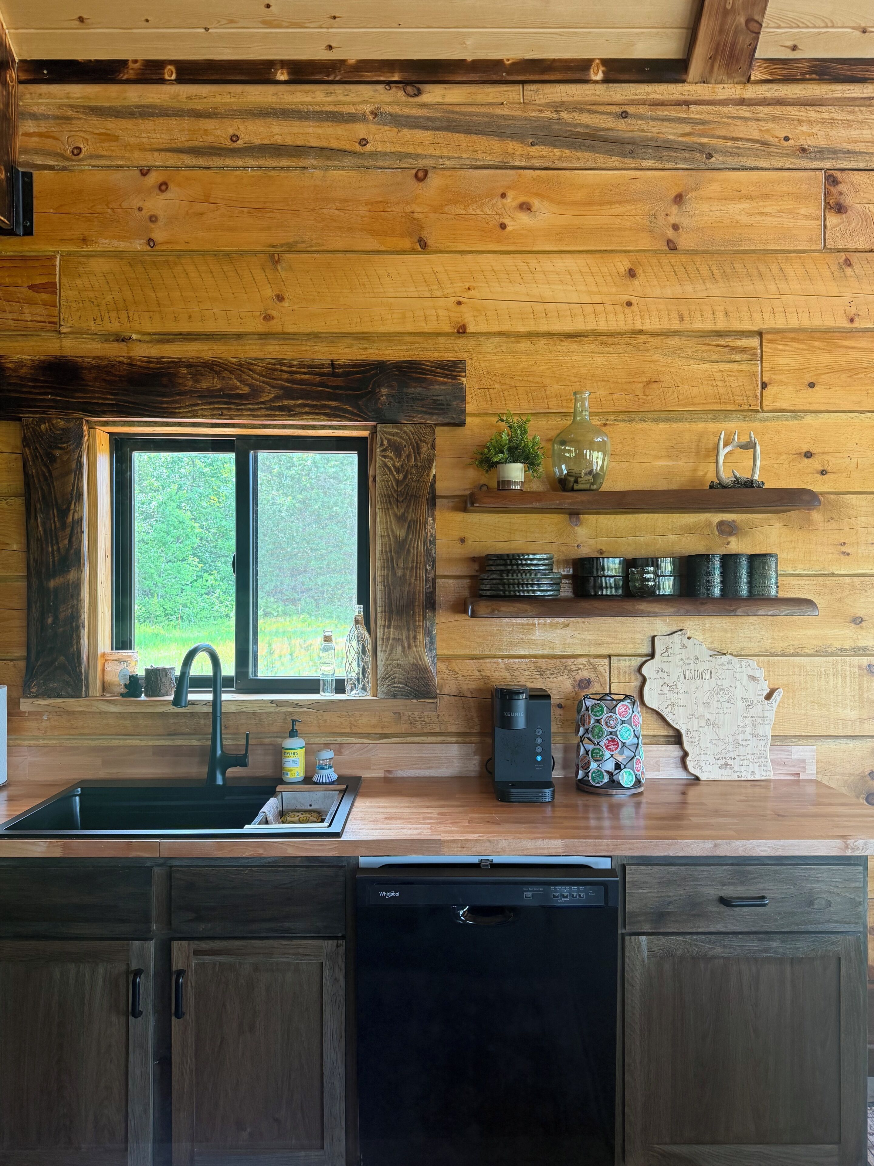 A kitchen with wooden walls, a window, a sink, a coffee maker, and a map decoration.