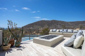 Eine Dachterrasse mit einem Steinkamin, einer Couch mit Kissen, Topfpflanzen und Blick auf eine gebirgige Landschaft.