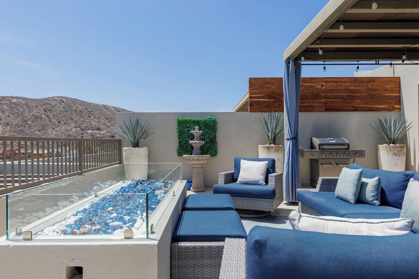 Une terrasse sur le toit avec une piscine à débordement en verre, des meubles d’extérieur bleus, un barbecue et un mur décoratif.