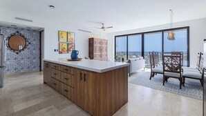 A modern kitchen with a large island, wooden cabinets, and a dining area with a view. - Modern 4BR Villa with Rooftop & Pickleball (Los Barriles)