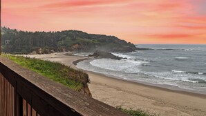A beach with a wooden boardwalk, ocean waves, and a forested hill. - Sunset Haven (Depoe Bay)