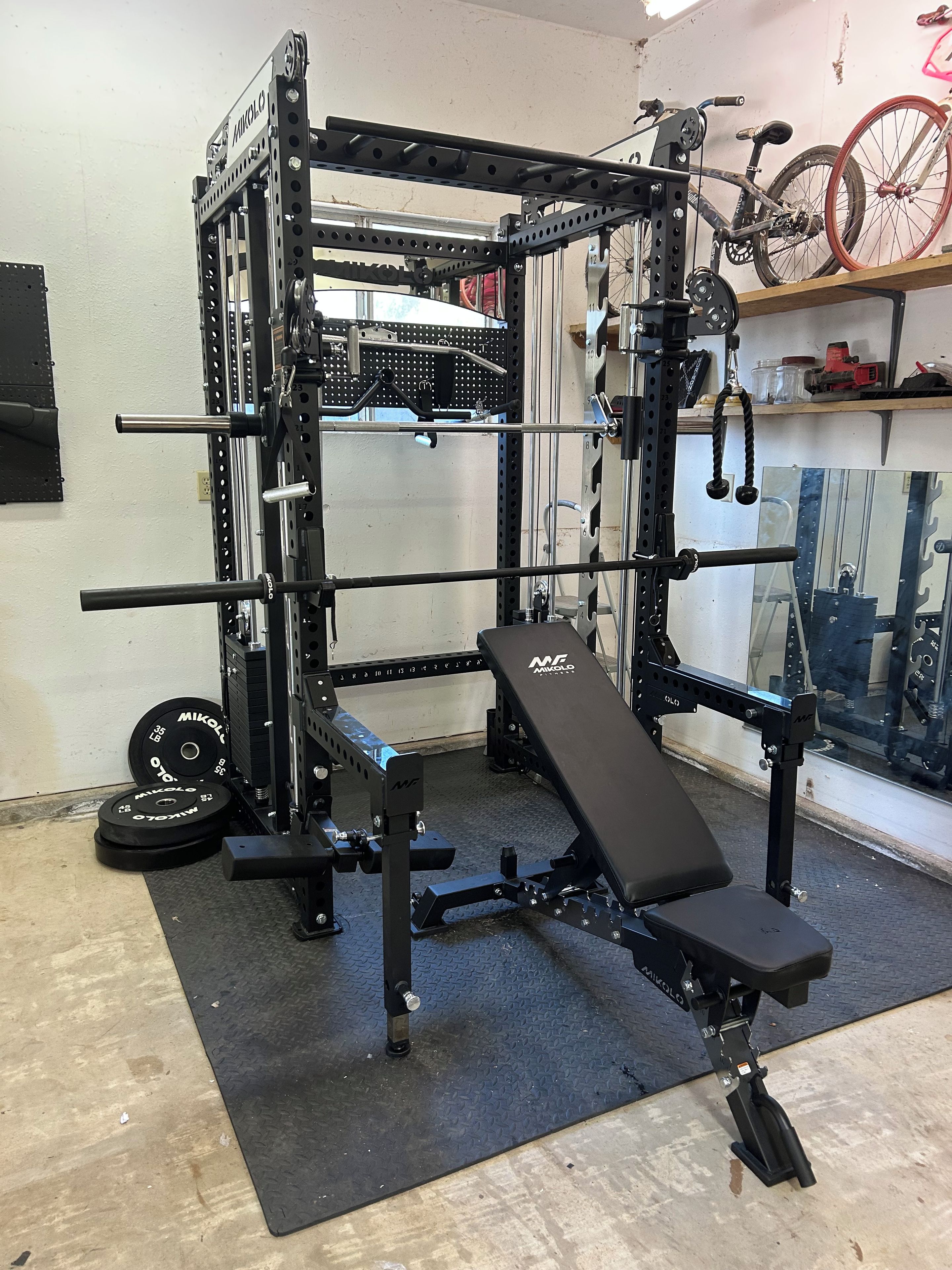 Ein Fitnessraum mit einem Squat-Rack, einer Bankpresse und Gewichtsplatten.
