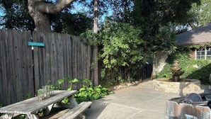 A wooden fence, a picnic table, and a stone fountain in a garden area.