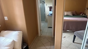 A hotel room with a bed, a small table, a chair, a mirror, and a bathroom visible through an open door.