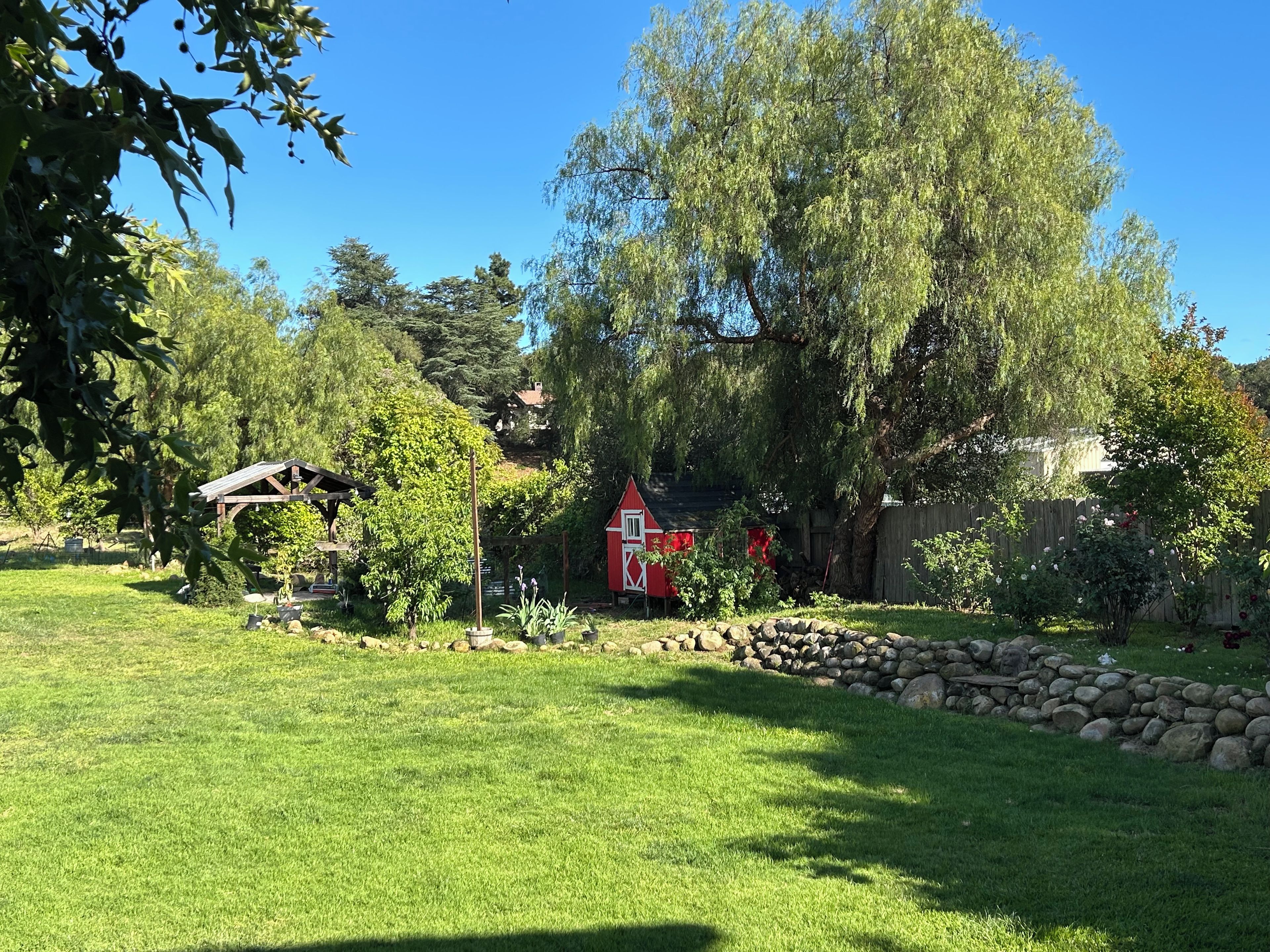 A well-maintained garden with a red barn, a wooden structure, and a stone wall.