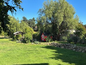 A well-maintained garden with a red barn, a wooden structure, and a stone wall. -   1-bedroom 1 bath suite on farmhouse property next to water fountain (Ojai)