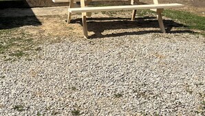 Een picknicktafel in een park met een grindpad, omringd door bomen en betonnen palen.