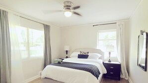 A bedroom with a bed, a nightstand, a lamp, a ceiling fan, and a window with curtains. - Relaxing Ranch Home in Eastlake (Atlanta)