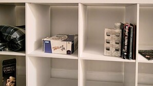 A white shelving unit with a flat-screen TV above it, a metallic water bottle, a box of tissues, a book titled 'Unfinished Glenjones,' and a small figurine. - Relaxing Ranch Home in Eastlake (Atlanta)