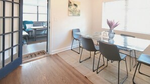 A modern meeting room with a glass table, four chairs, a vase with purple flowers, a painting on the wall, and a view through a glass door. - Relaxing Ranch Home in Eastlake (Atlanta)