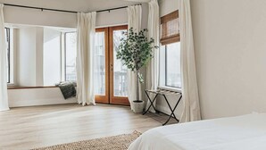 A bedroom with a bed, a window with curtains, a plant, and a radiator. - Bearfoot Lake Escape (Big Bear Lake)