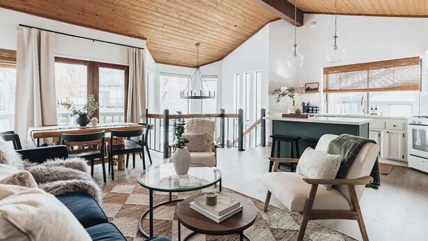 A spacious living area with a high ceiling, a dining table, a kitchen, and a cozy seating area. - Bearfoot Lake Escape (Big Bear Lake)