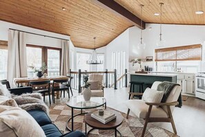 Een ruime woonkamer met een hoge plafond, een eettafel, een keuken en een gezellige zithoek.