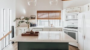 A modern kitchen with white cabinetry, a central island, a stove, and a refrigerator. - Bearfoot Lake Escape (Big Bear Lake)