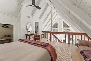 Ein Schlafzimmer mit einem großen Bett, einem Deckenventilator aus Holz, einem Schachbrettteppich und einem Balkon mit hölzernem Geländer.