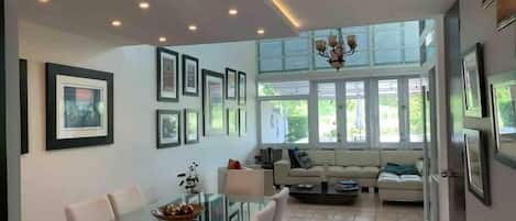 A modern living room with a glass dining table, white sofas, and framed pictures on the walls.