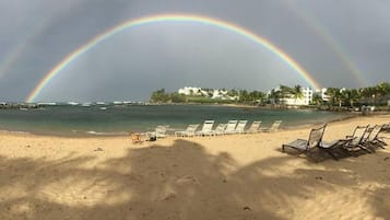 Una playa con sillas de descanso, cielo despejado y un arcoíris.