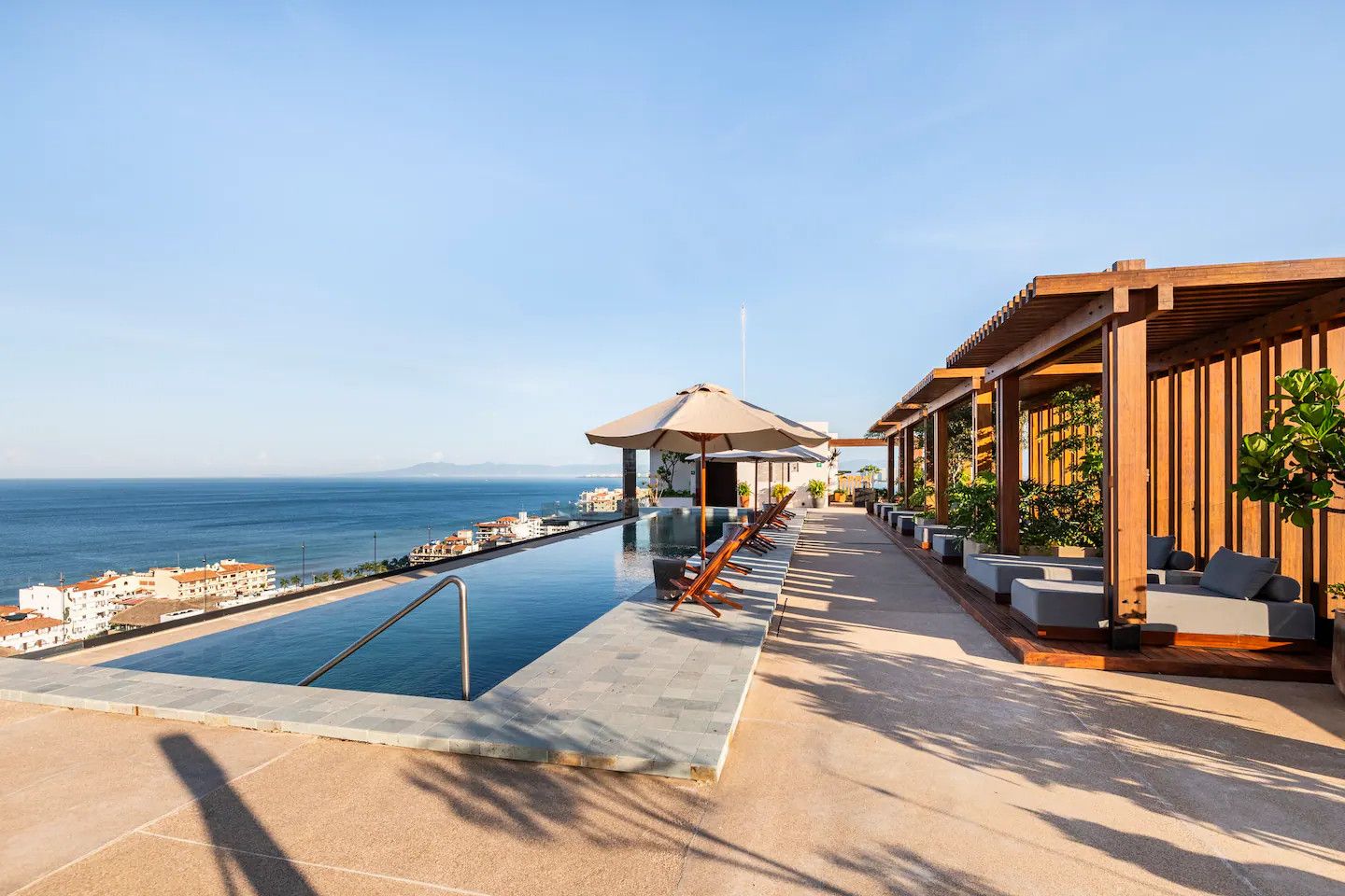 A poolside area with a view of the sea, outdoor seating, and a covered structure.