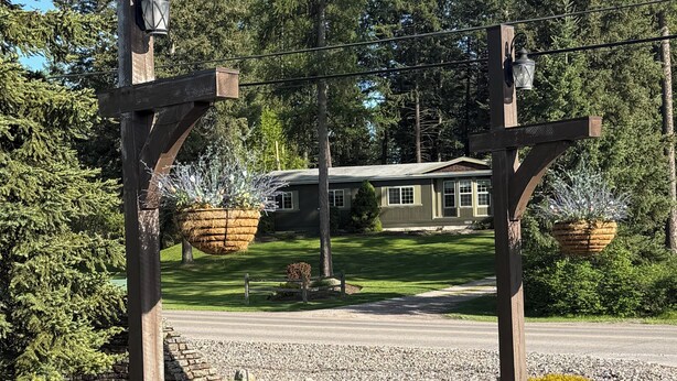 Una pergola in legno con lanterne appese e piante in vaso, un vialetto lastricato e una casa sullo sfondo.