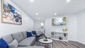 Un salon moderne avec un canapé gris, des coussins bleus, une table basse ronde et une étagère blanche agrémentée d’objets décoratifs.