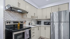 Une cuisine moderne dotée d’appareils électroménagers en acier inoxydable, d’une cuisinière à gaz, d’un four encastré et de meubles de rangement blancs.