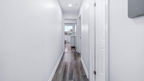 Un couloir étroit aux murs blancs et au plancher en bois mène à un espace cuisine.