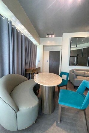 A modern room with a round table, teal chairs, a grey sofa, and a large mirror on the wall. - Convenient City Escape at One Madison Towers (Iloilo City)