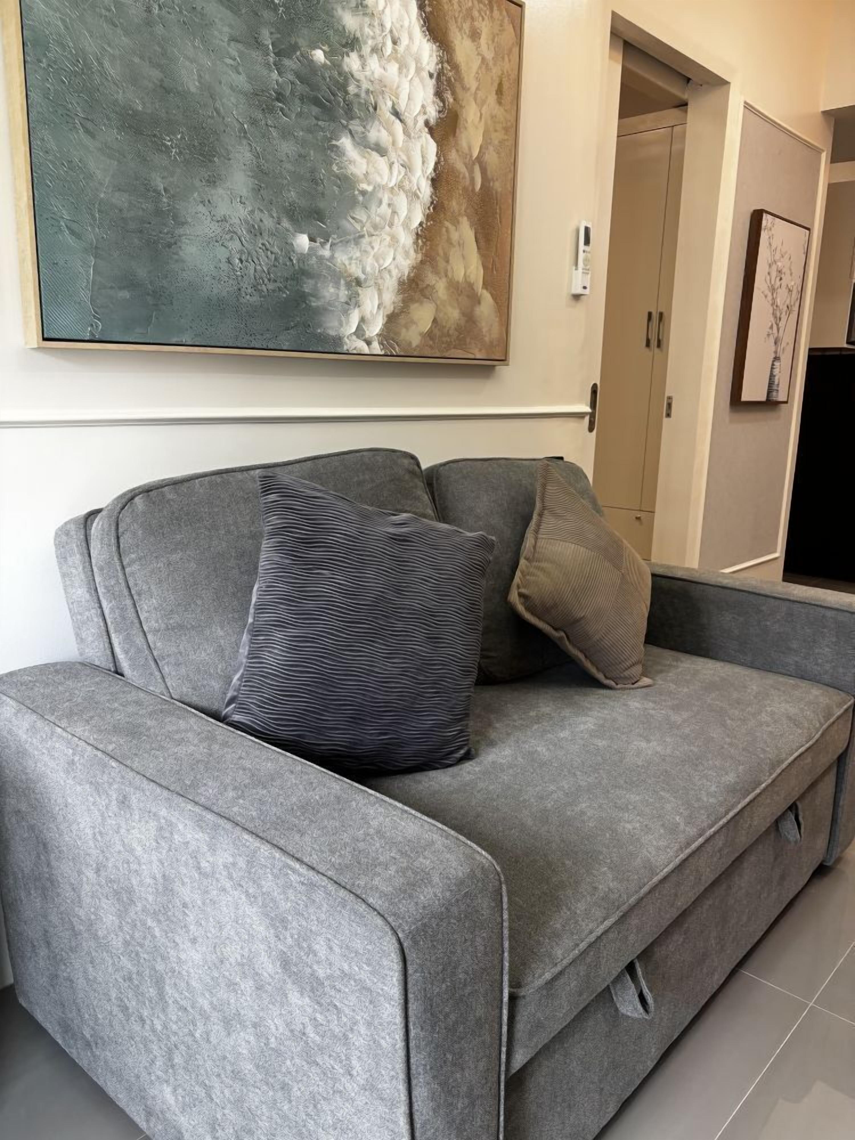 A grey sofa with two pillows, a large abstract painting, and a door in the background.