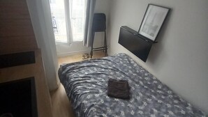 A bedroom with a bed, a chair, a TV, and a window with curtains. - Cosy mini studio in Montmartre (Paris)