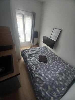 Ein Schlafzimmer mit Bett, Sessel, Fernseher und einem Fenster mit Vorhängen.