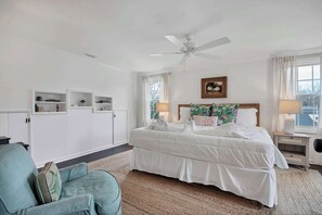 A bedroom with a bed, a ceiling fan, a nightstand, a lamp, a chair, and built-in shelves.
