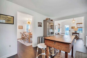 A spacious kitchen with a wooden table, wicker bar stools, and a cabinet with glass doors.