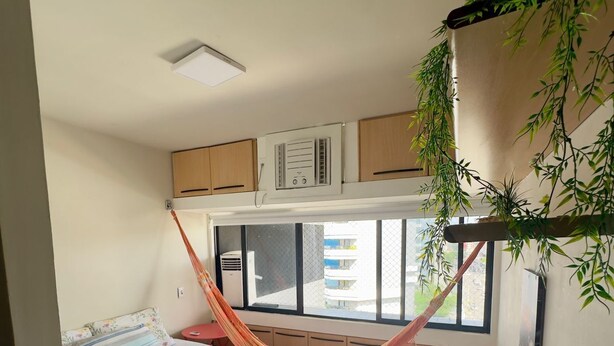 Un dormitorio con cama, ventana, radiador y una planta colgante.