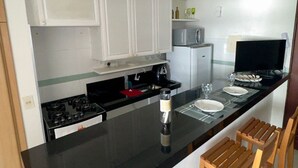 Una cocina moderna con armarios blancos, encimera negra, estufa y un comedor con dos sillas de madera.