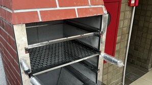 Un horno exterior de ladrillo con tres repisas y un asa metálica.