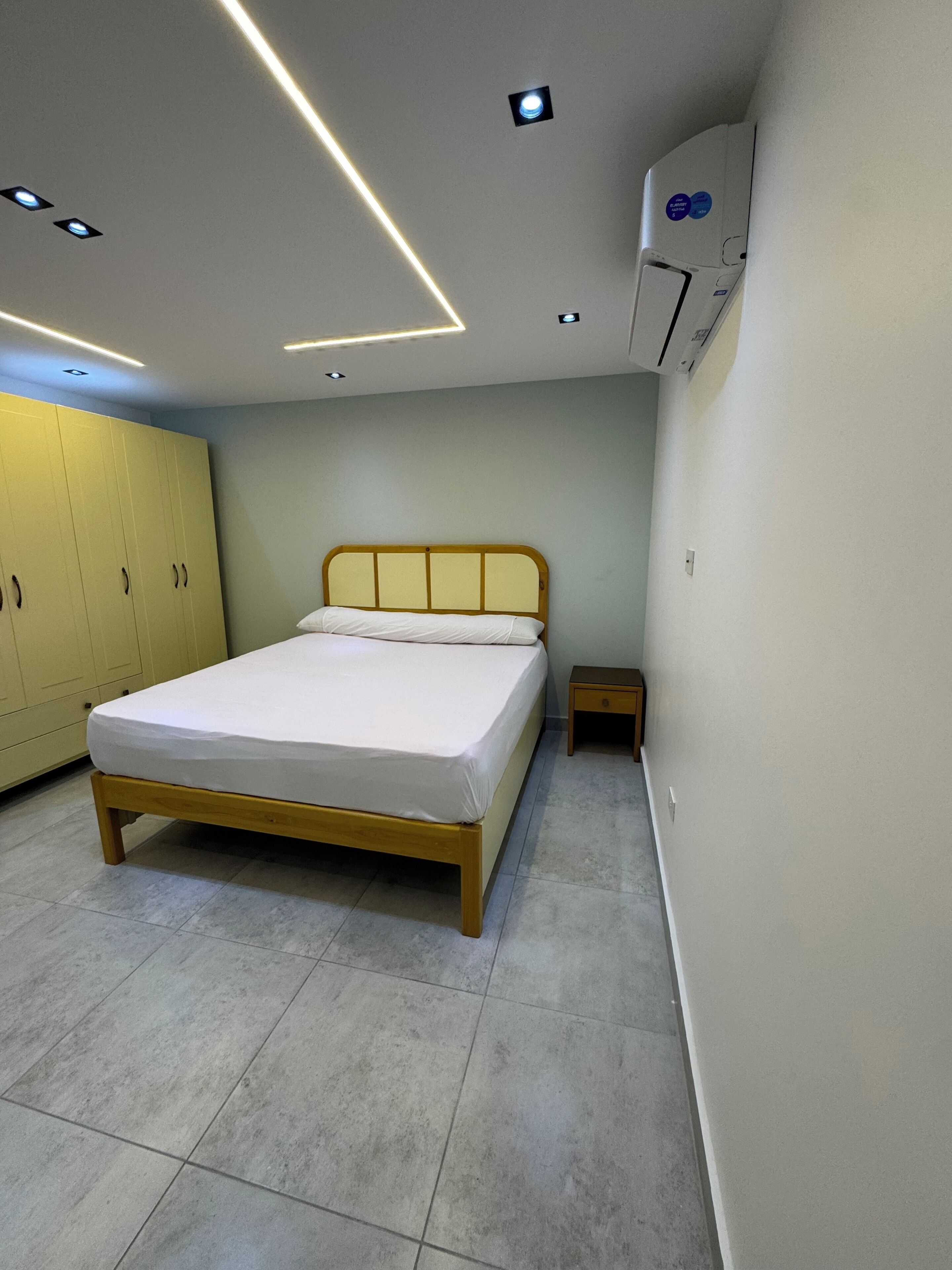 Un dormitorio con cama, armario, mesita de noche y aire acondicionado.