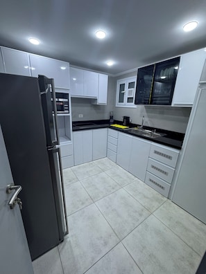 A modern kitchen with white cabinets, a stainless steel refrigerator, and a black countertop. - Panoramic Sea View Apartment – Port Said (محافظة بورسعيد)