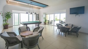 Um espaço amplo e interno com mesa de bilhar, móveis de vime e uma televisão fixada na parede.