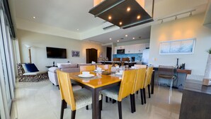 Uma sala de jantar moderna com uma mesa de madeira, cadeiras e uma cozinha ao fundo.