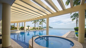 Uma piscina com hidromassagem, palmeiras e vista para o oceano.