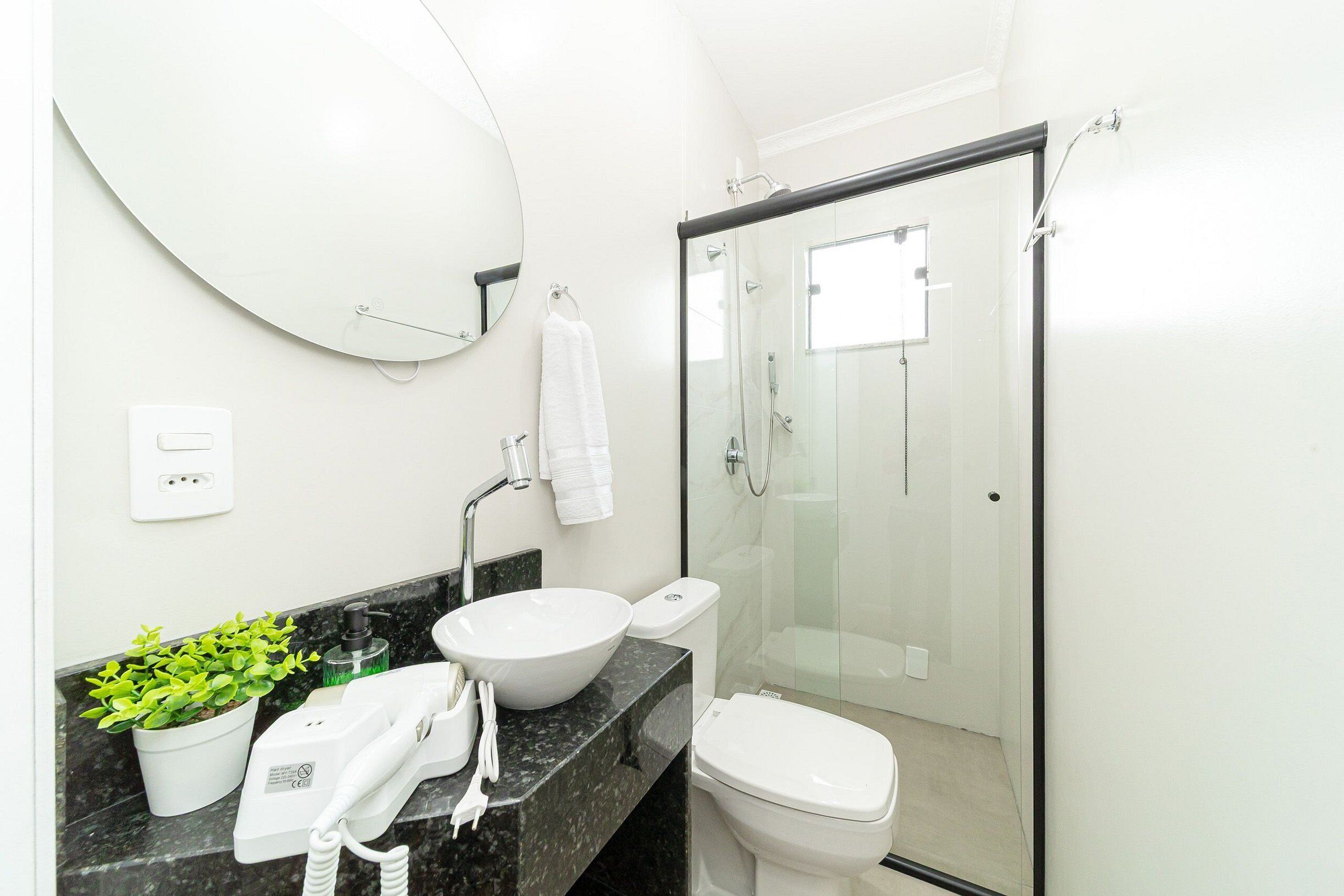Une salle de bain moderne avec un grand miroir rond, un lavabo blanc en forme de cuvette, des toilettes et une douche à parois de verre.