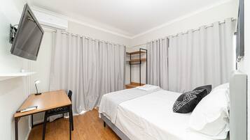 A bedroom with a bed, a desk, a TV mounted on the wall, and a shelf unit.
